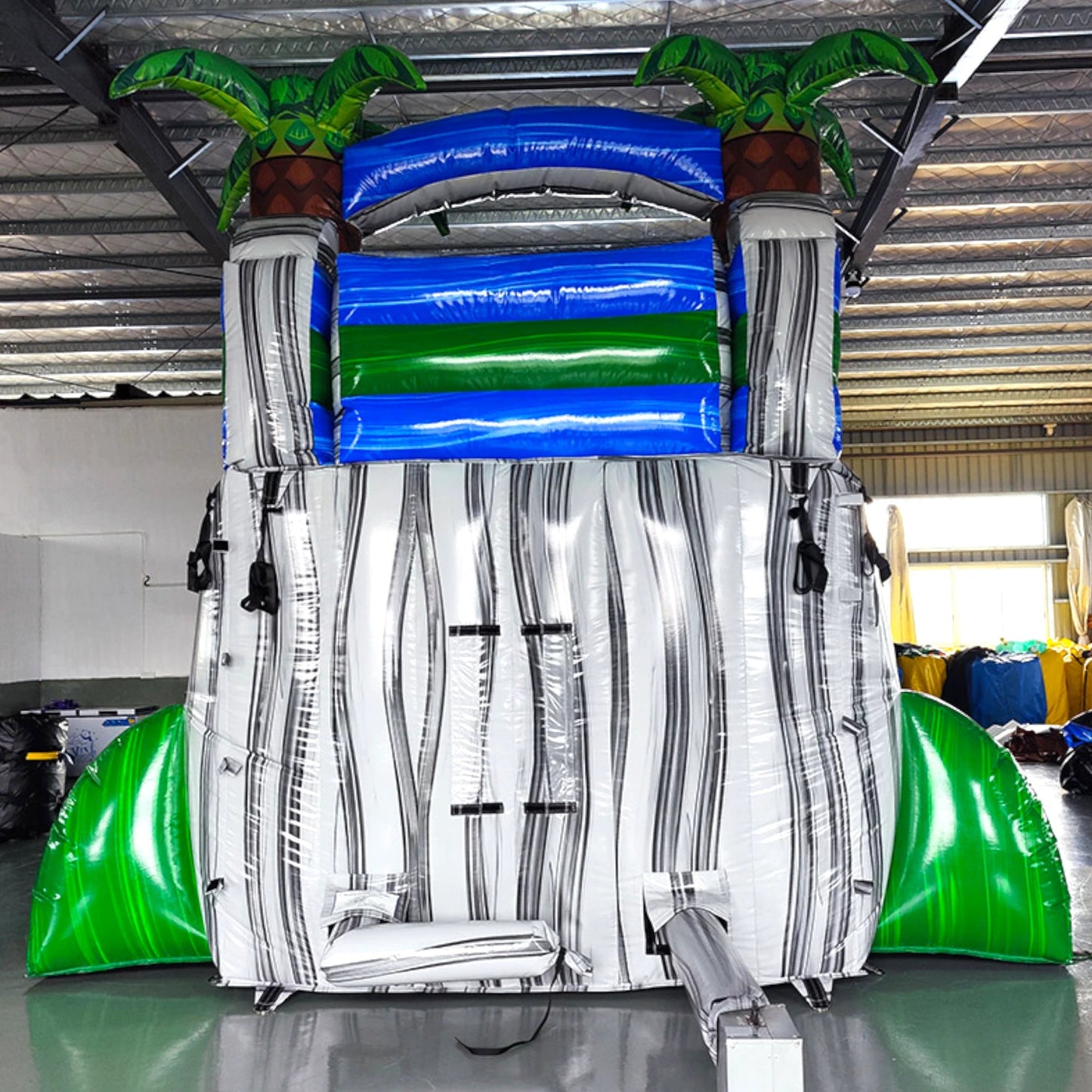 Rear view of Aloha Splash single lane water slide, showcasing tall white structure with climbing area, safety features, and tropical-themed top section with palm trees.