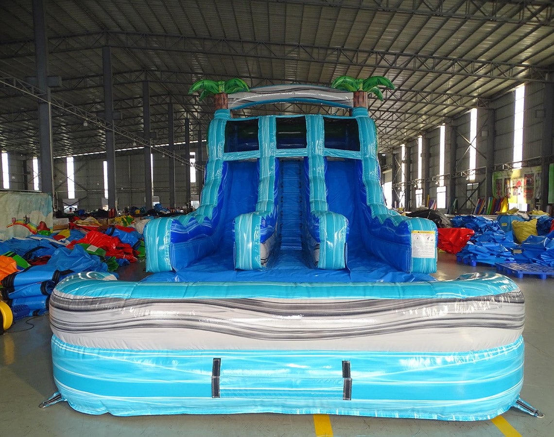 Front view of the 15ft Bahama Blast water slide showing three blue sliding lanes, central climbing section, inflatable palm trees on top, and a large splash pool area at the base.