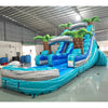 Side view of Bahama Blast inflatable water slide displaying full length with blue sliding lane, palm tree accents, and spacious splash pool in warehouse environment.