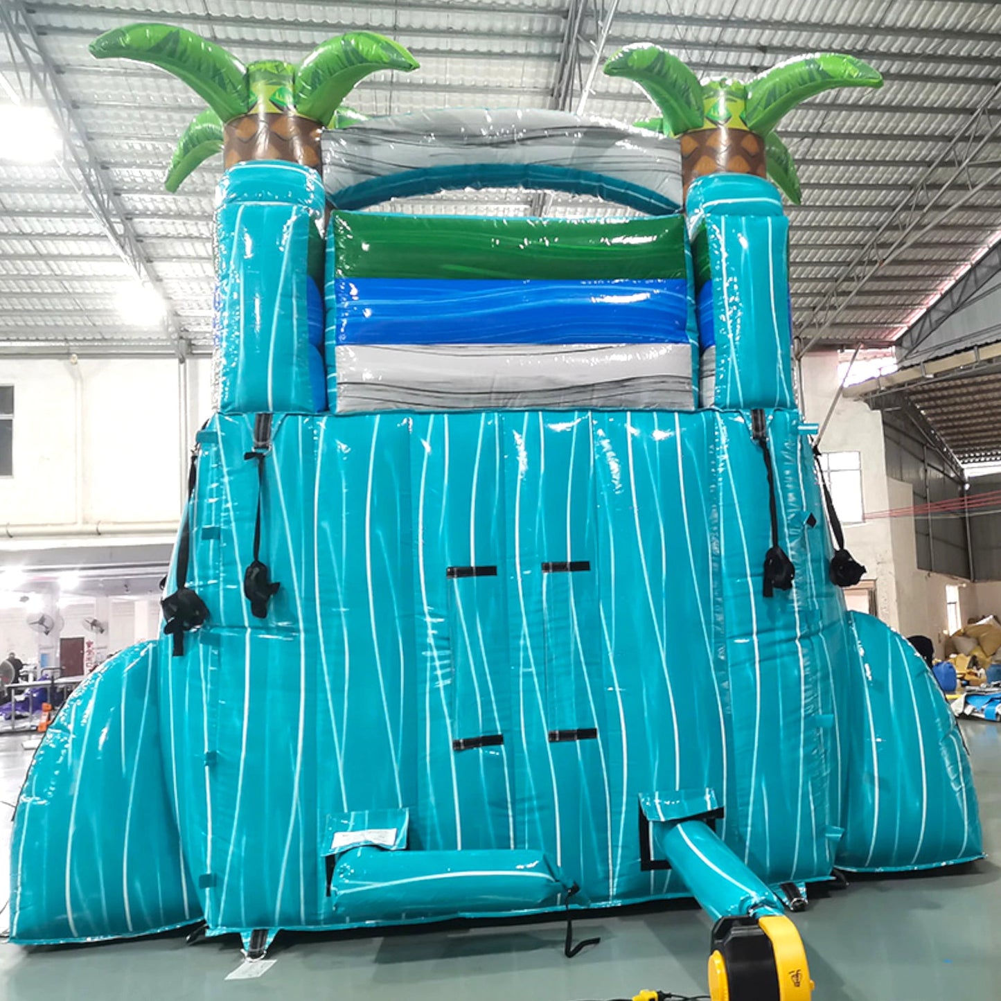 Rear view of Bahama Blast single lane water slide, showcasing tall turquoise structure with climbing area, safety features, and tropical-themed top section with palm trees.