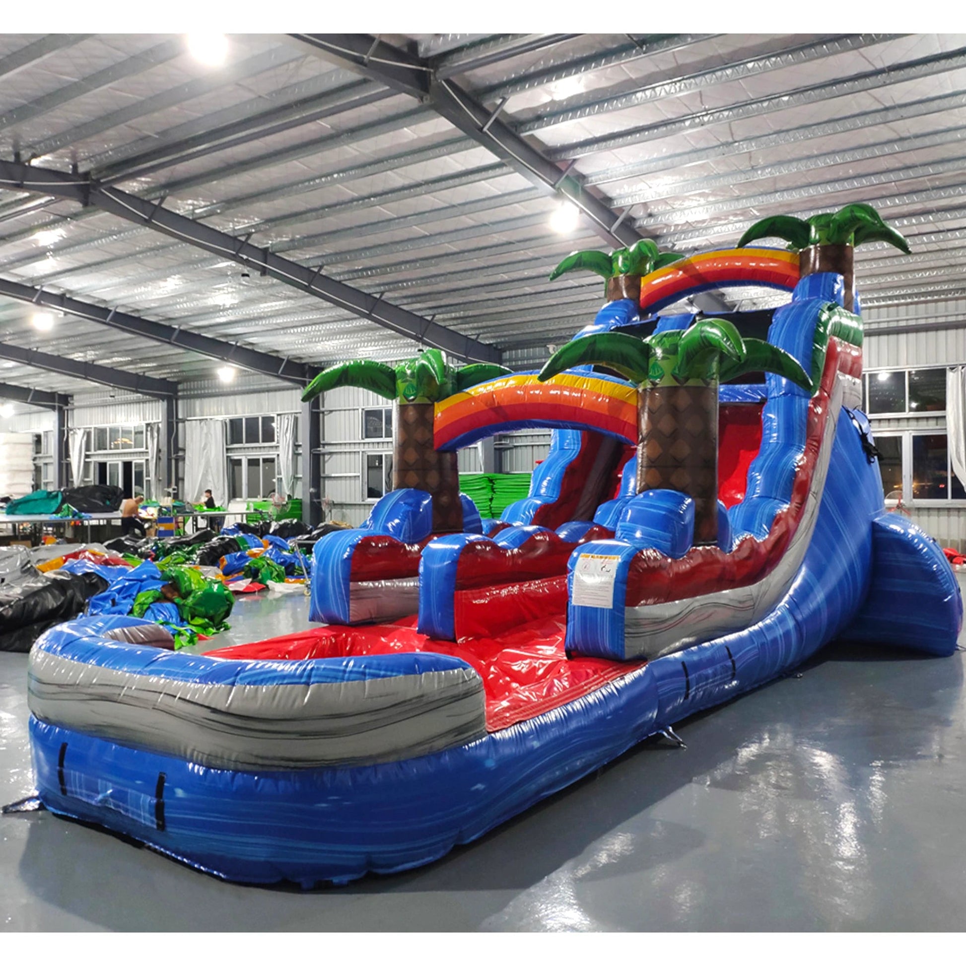 Side view of Baja Splash inflatable water slide displaying full length with blue sliding lane, palm tree accents, and spacious splash pool with wave-like design.