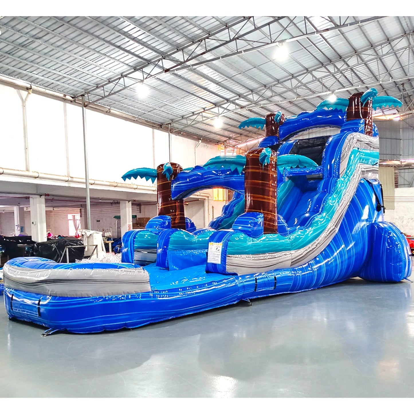 Front angled view of Cayman Crush single lane water slide in indoor facility, showcasing its height, blue sliding lane, palm tree decorations, and extended splash pool area.