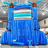 Rear view of Cayman Crush inflatable water slide, displaying tall blue structure with climbing area, safety features, and tropical-themed top section with palm trees.