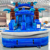 Large tropical-themed inflatable water slide featuring a single blue sliding lane, palm tree decorations, and an extended splash pool with wave-like design in indoor warehouse setting.