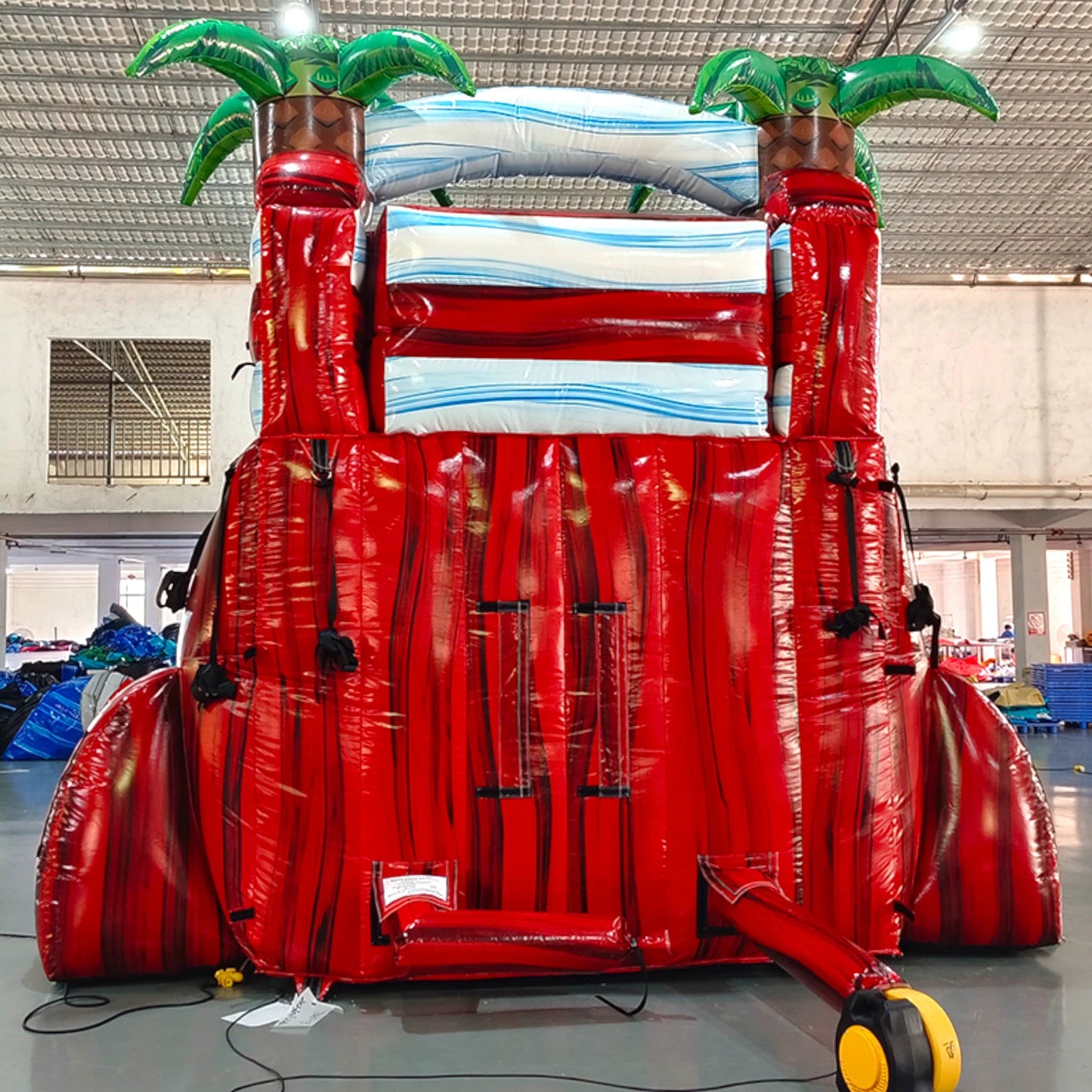 Rear view of Crimson Bay single lane water slide, showcasing tall red structure with climbing area, safety features, and tropical-themed top section with palm trees.