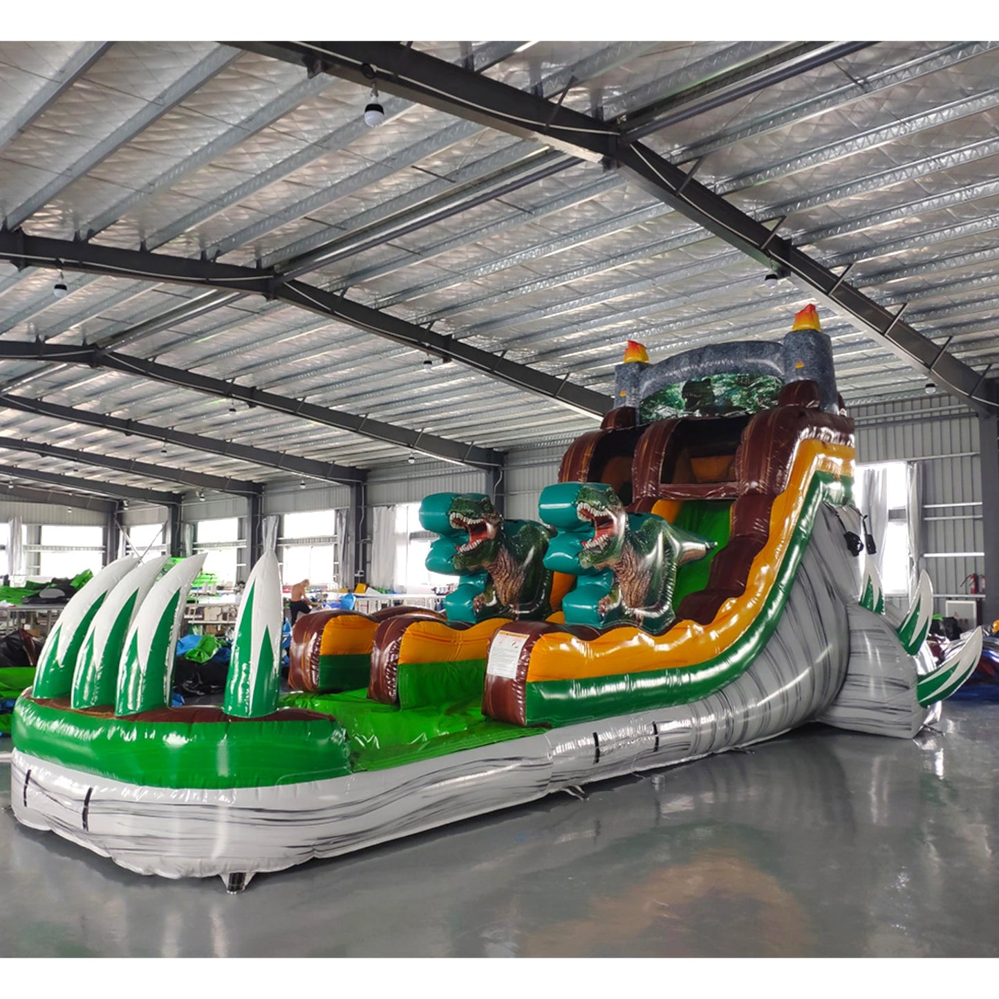 Side view of Dino Dive inflatable water slide displaying full length with dinosaur figures, single sliding lane, and green splash pool area in indoor facility.