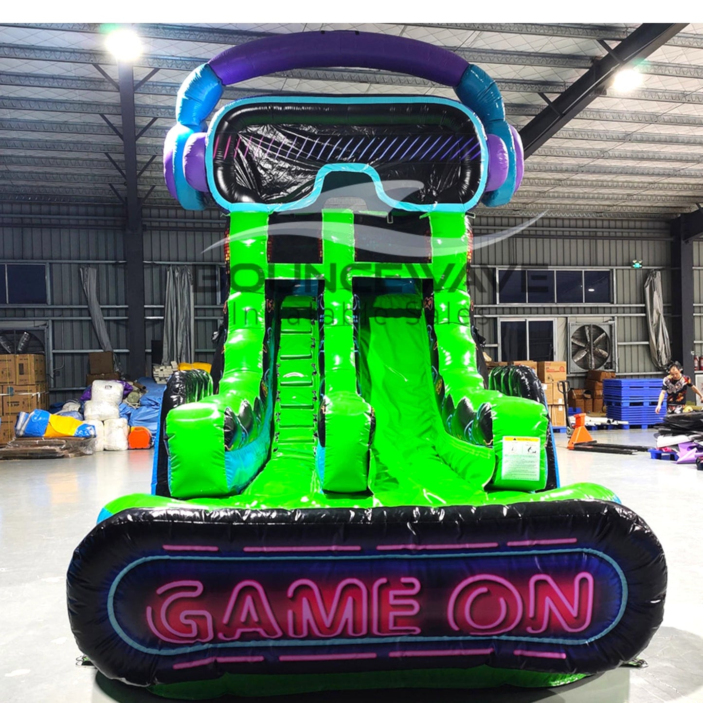 Front view of Game Wave inflatable water slide displaying vibrant green design, single lane, VR headset decoration on top, and spacious splash pool with "Game On" sign in indoor facility.