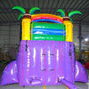 Rear view of tropical-themed inflatable water slide with palm tree decorations, showing tall purple structure and colorful top section in indoor warehouse setting.