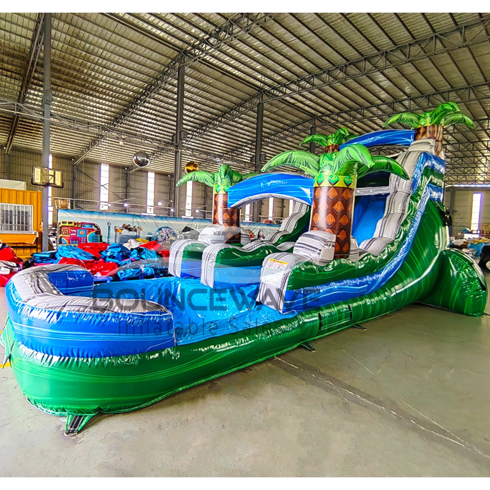 15ft Green Gush Commercial Single Lane Inflatable Water Slide showcasing blue slide, inflatable palm trees, and extended green splash pool in warehouse setting
