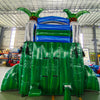 15ft Green Gush Commercial Single Lane Inflatable Water Slide featuring tropical palm trees, blue curved slide, and green inflatable base with extended splash pool in warehouse setting