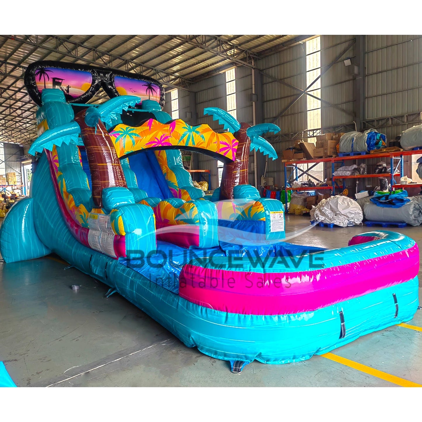 Side view of Island Flow single lane water slide featuring turquoise base, sunglasses-shaped top, palm tree decorations, and extended splash pool with pink rim.