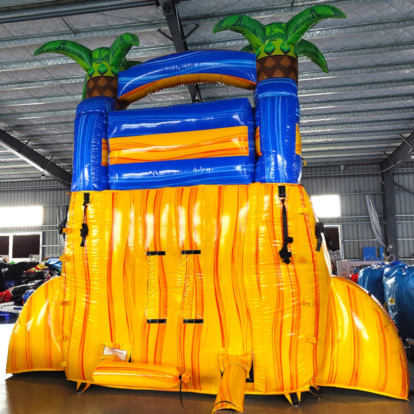 Rear view of Lava Falls single lane water slide, showcasing tall yellow structure with climbing area, safety features, and tropical-themed top section with palm trees.