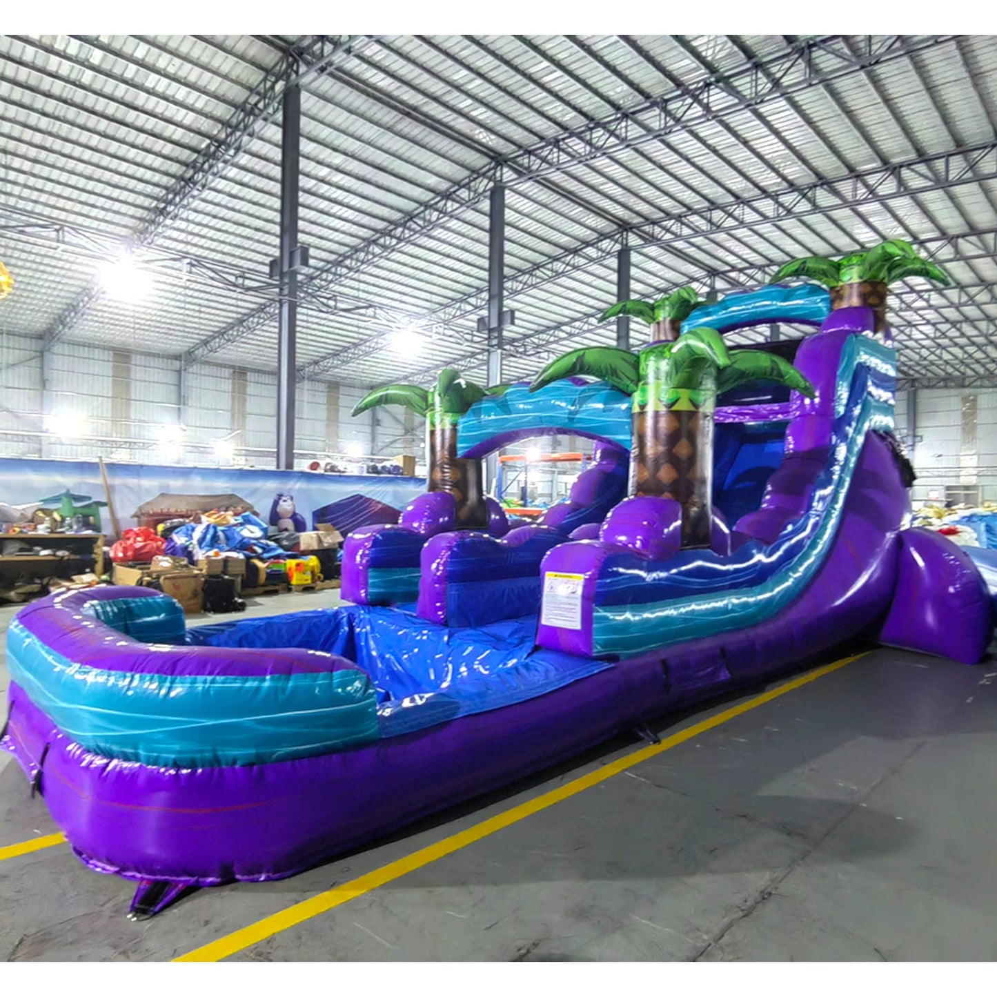 Side view of Purple Plunge single lane water slide in indoor facility, showcasing its length, purple sliding lane, palm tree decorations, and extended blue and purple splash pool area.