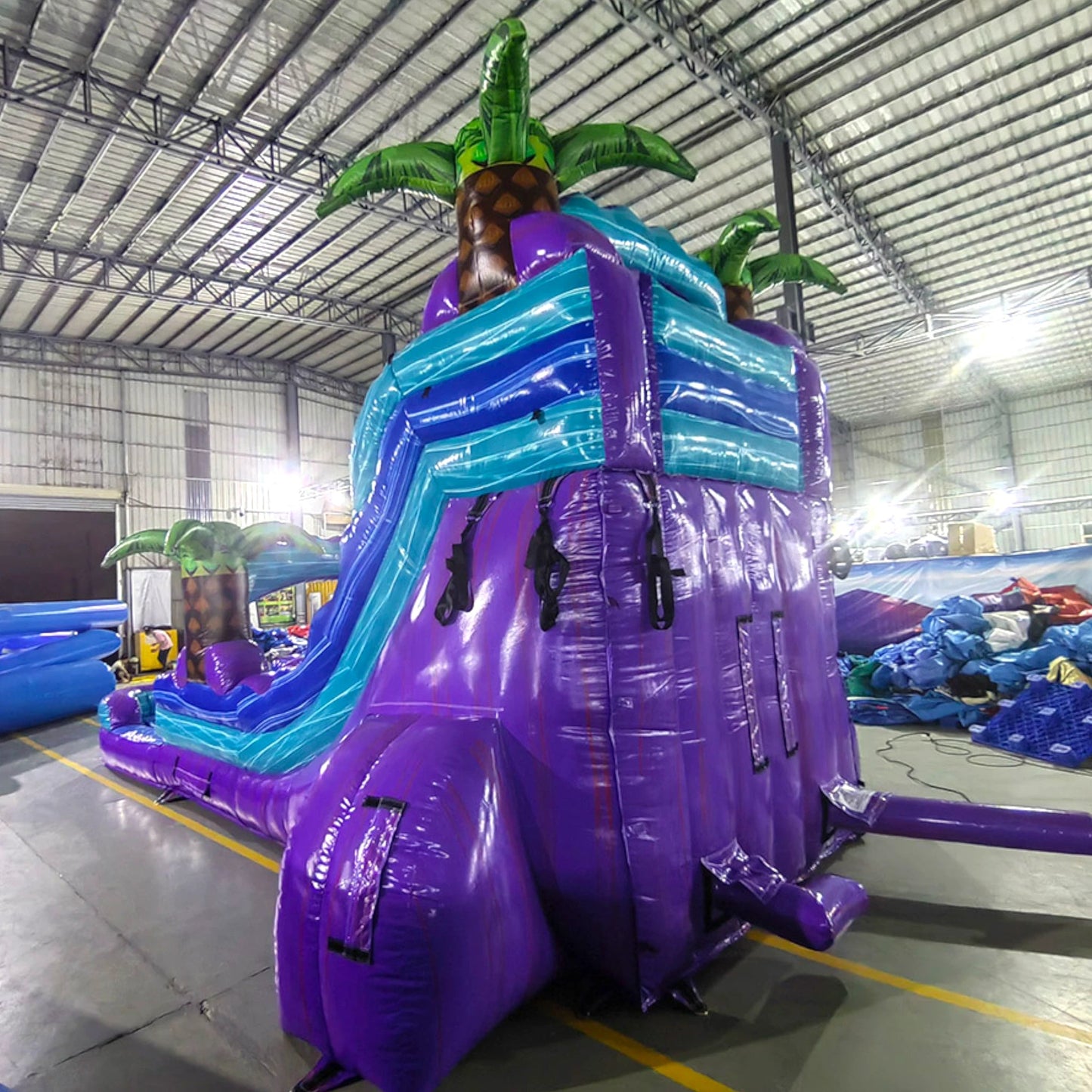 Rear view of Purple Plunge inflatable water slide, displaying tall purple structure with climbing area, safety features, and tropical-themed top section with palm trees.