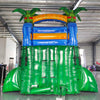 Rear view of Reggae Rush inflatable water slide, displaying tall green structure with climbing area, safety features, and tropical-themed top section with palm trees and tiki designs.