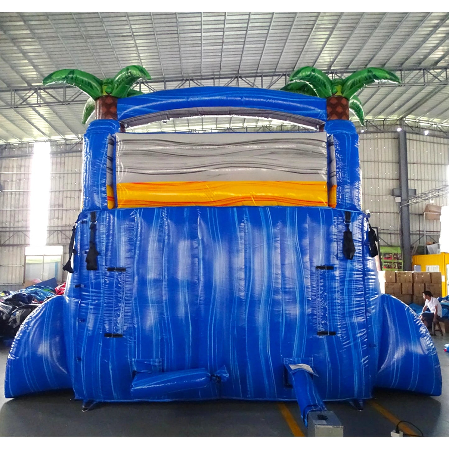 15ft Rip Curl Dual Lane Center Climb Inflatable Water Slide featuring blue structure, dual red slides, inflatable palm trees, and colorful splash pool in warehouse setting