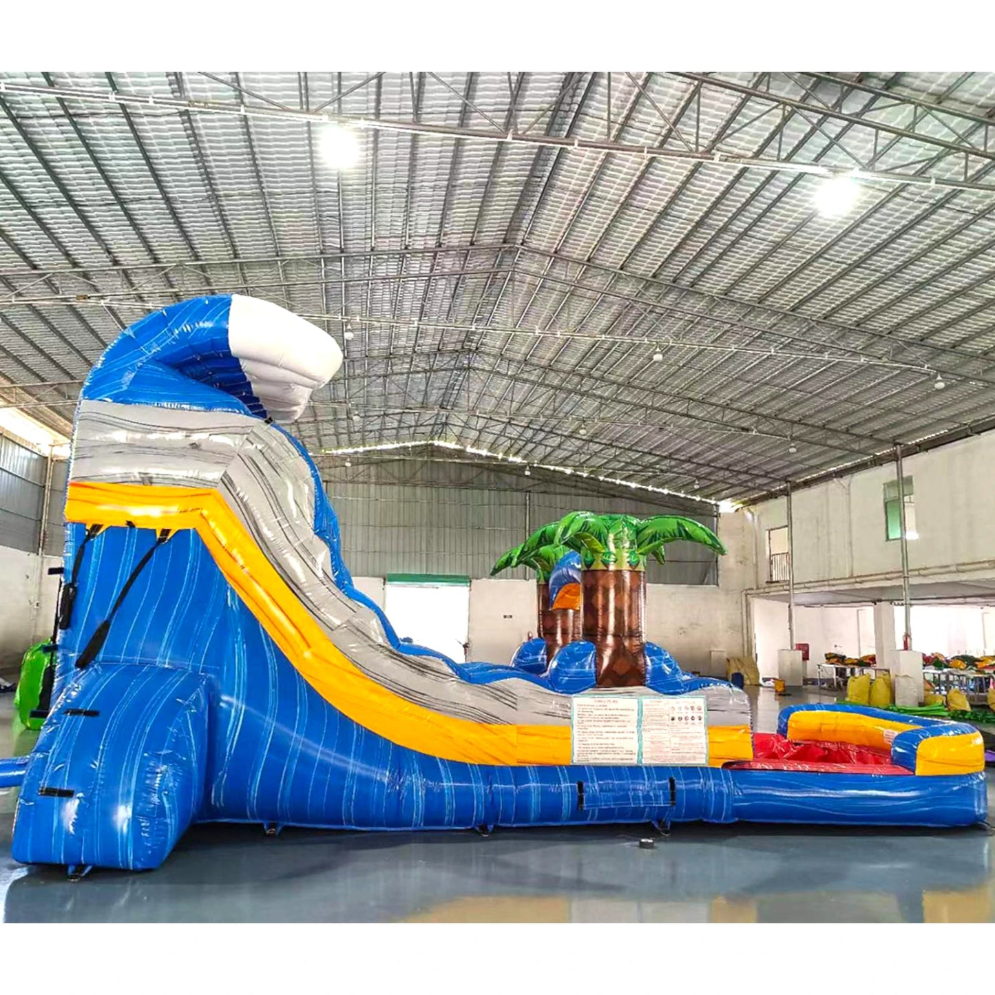 Side view of Rip Curl inflatable water slide displaying full length with blue sliding lane, palm tree accents, and spacious splash pool in indoor facility.