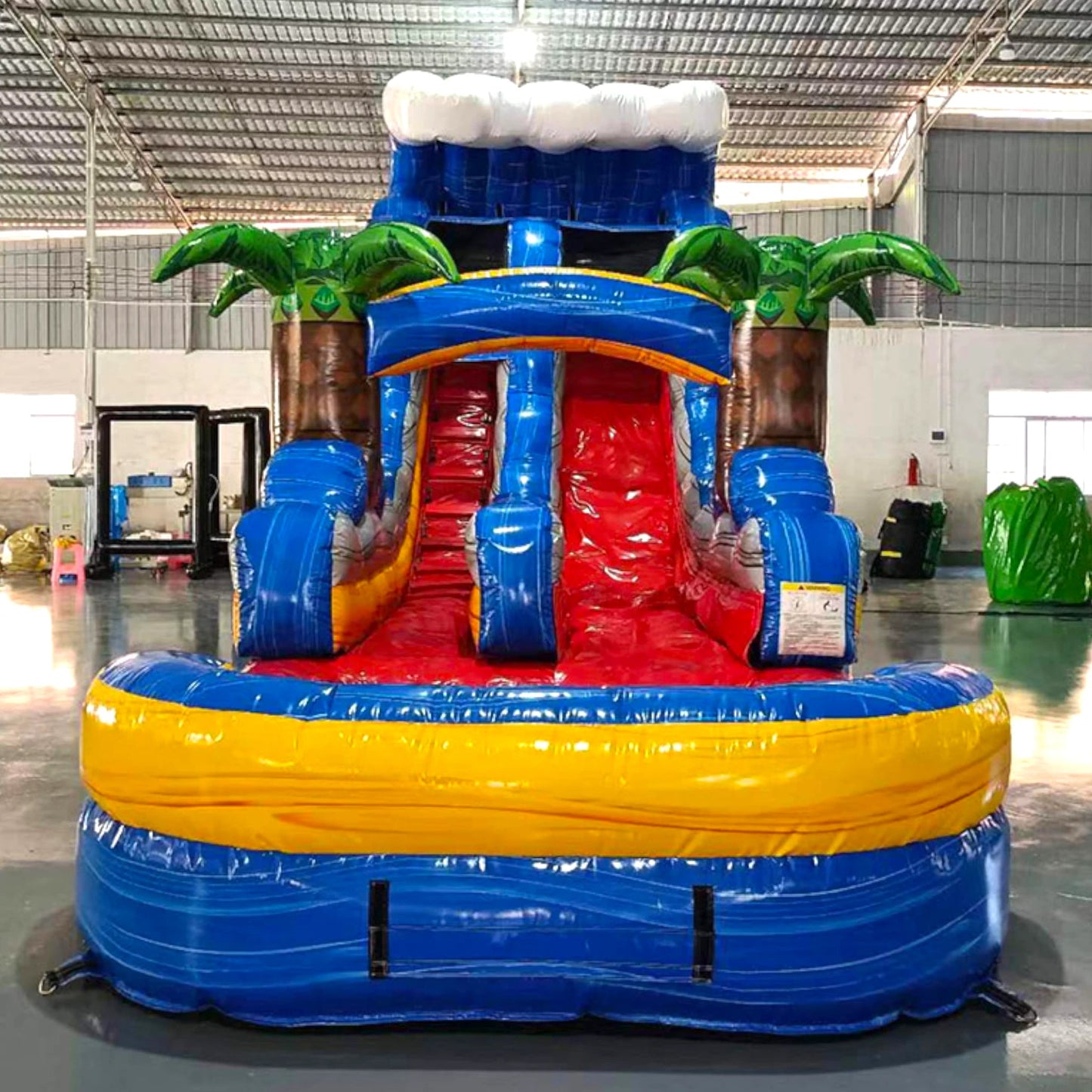 Front view of Rip Curl single lane water slide showcasing its height, blue sliding surface, palm tree decorations, and extended splash pool area with yellow rim.