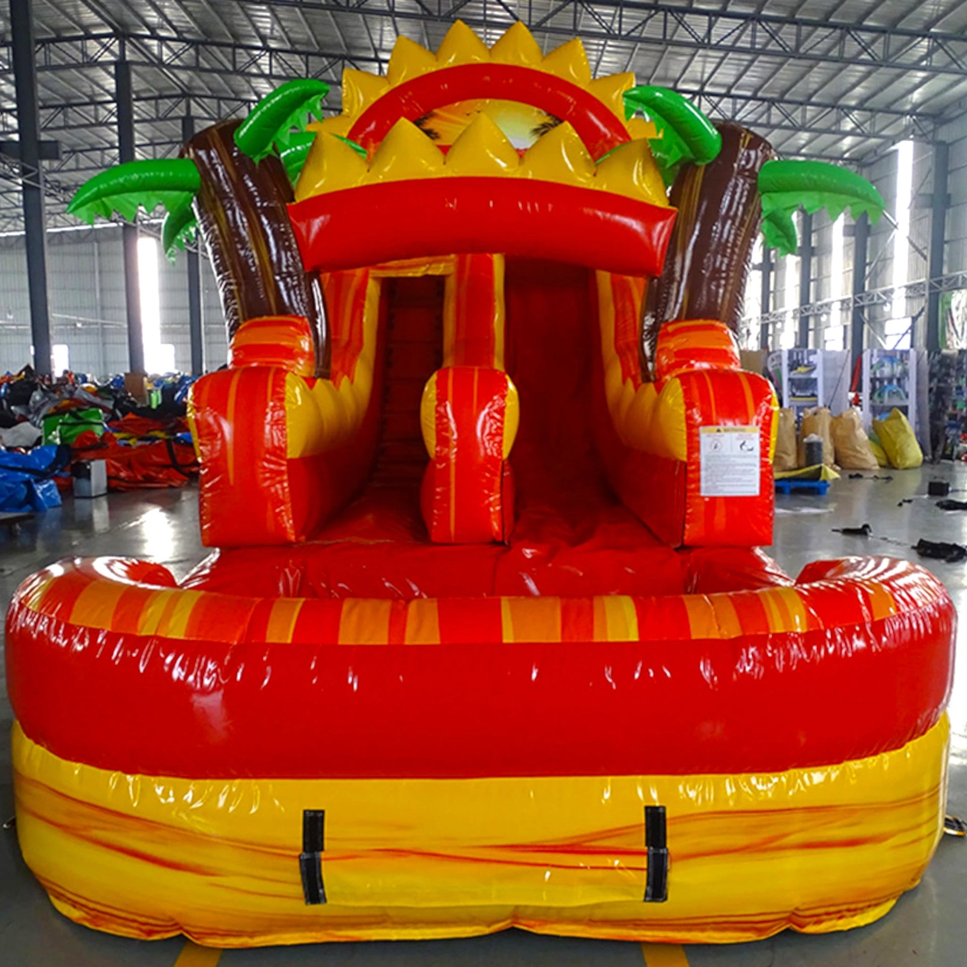 Front view of Summer Sizzler inflatable water slide displaying vibrant yellow and red design, single lane, sun and palm tree decorations, and spacious splash pool in indoor facility.