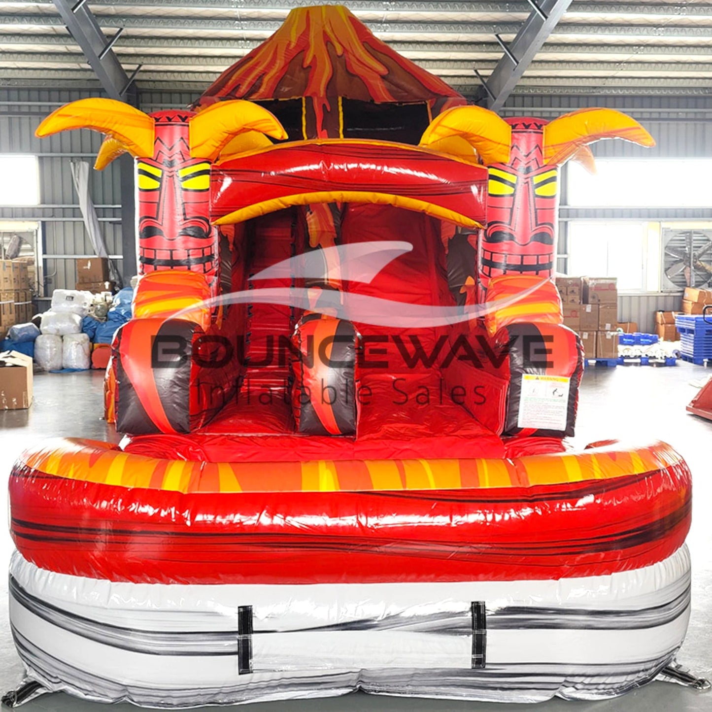 Front view of Tiki Volcano inflatable water slide displaying vibrant red and orange design, single lane, tiki mask decorations, and spacious splash pool with lava-themed elements.