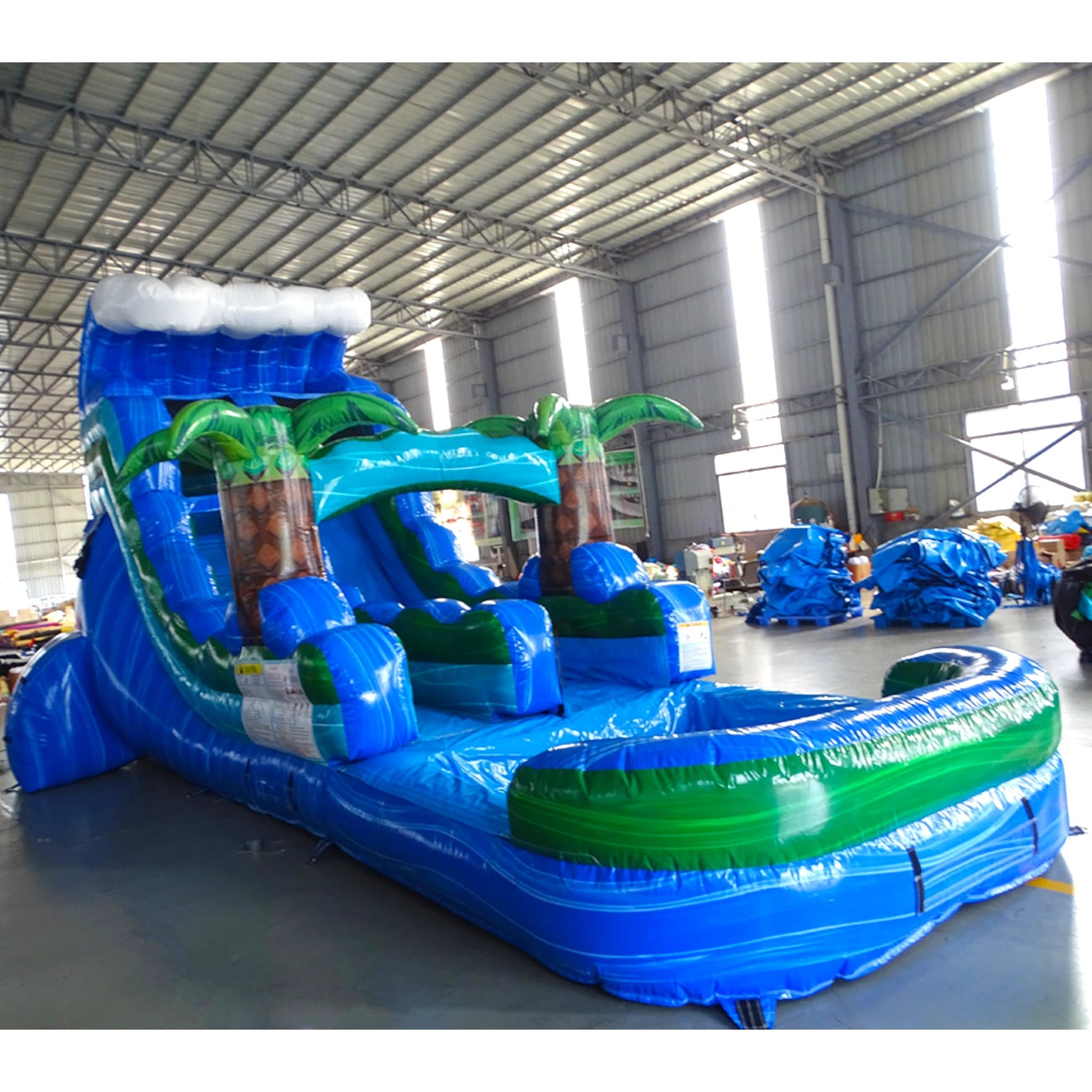 Side view of Trop Wave single lane water slide showing full length with blue sliding surface, palm tree accents, and large splash area with blue and green colors.