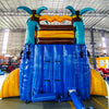 Inflatable tropical-themed water slide with blue base, teal palm trees, and yellow-orange top, featuring a single lane and set up in an indoor warehouse