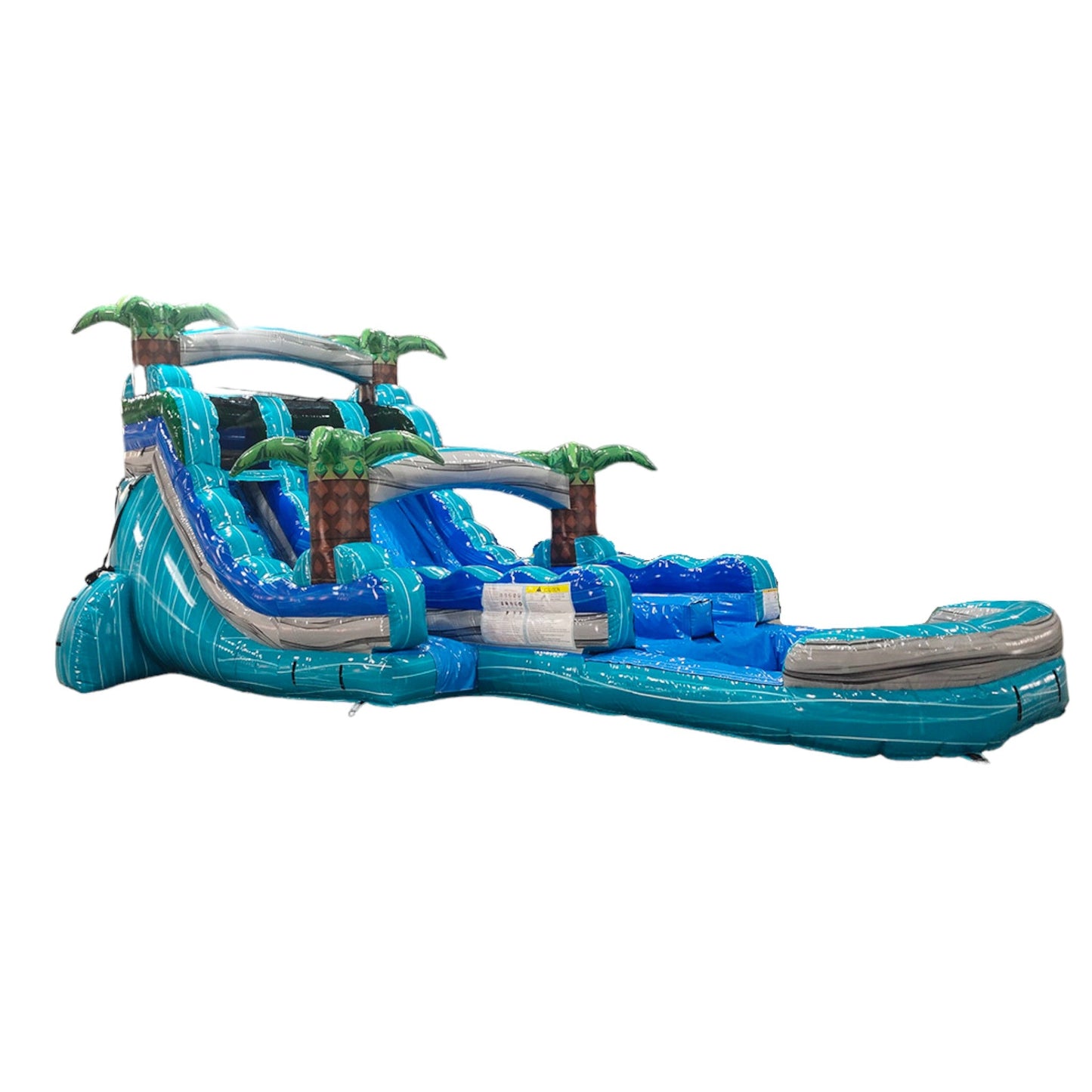 Side view of 16' Bahama Blast Hybrid DL water slide showing vibrant blue colors, inflatable palm trees, and a large splash pool area. The slide features both open and enclosed sliding sections, displayed in an indoor facility with metal roofing.