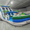 Three-quarter view of 18ft Aloha Splash water slide displaying blue lanes, green accents, inflatable palm trees, central climbing structure, and spacious splash area with tropical-themed design elements.