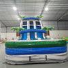 Front view of 18ft Aloha Splash inflatable water slide featuring three blue lanes, tropical palm tree decorations, central climbing structure, and large splash pool with green and blue accents.