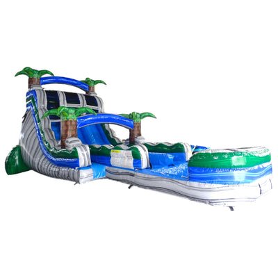 Large inflatable water slide with tropical theme, featuring a tall blue and gray structure with palm tree decorations, multiple sliding lanes, and a long splash pool. 