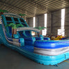 Three-quarter view of 18ft Bahama Blast water slide displaying blue lanes, tropical-themed design with palm trees, central climbing structure, and large splash area surrounded by other inflatable products in a warehouse.