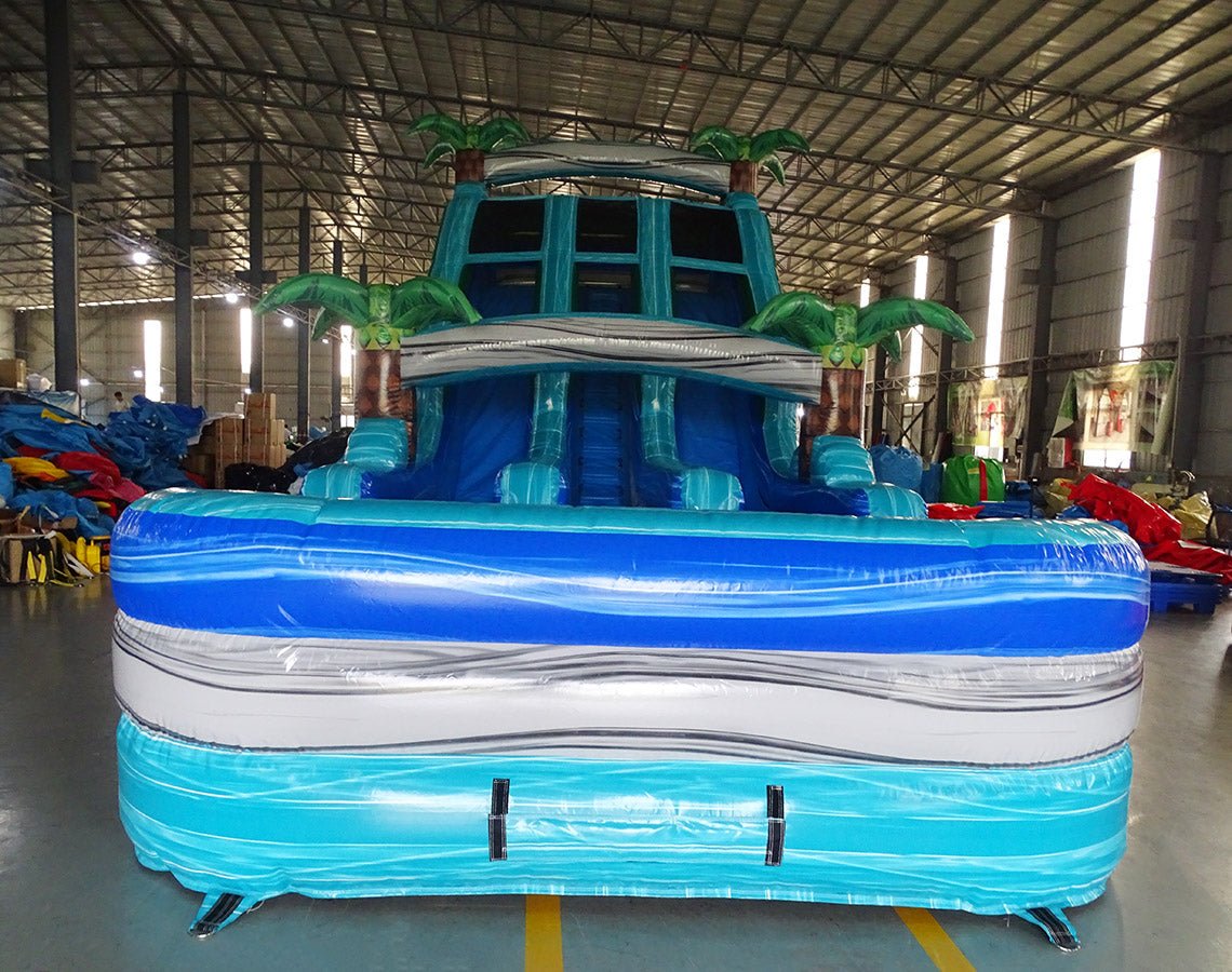 Front view of 18ft Bahama Blast Center Climb water slide showing three blue sliding lanes, inflatable palm trees, central climbing area with safety netting, and spacious splash pool area with blue and white color scheme.