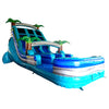 Side view of 18ft Bahama Blast inflatable water slide featuring three blue lanes, tropical palm tree decorations, central climbing structure, and large splash pool with wave-like patterns in an indoor warehouse setting.