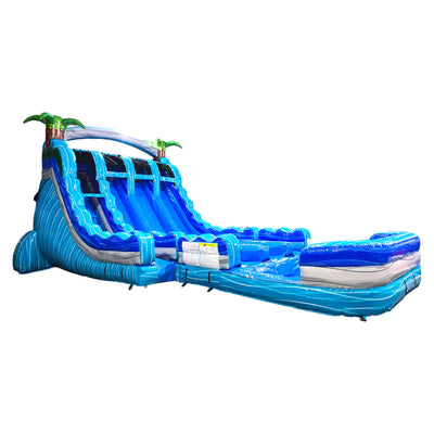 18-foot Bahama Blast inflatable water slide with triple lanes, featuring a tall blue and turquoise structure, palm tree decorations, and a large curved splash pool. This tropical-themed waterslide offers multiple sliding options for outdoor entertainment.