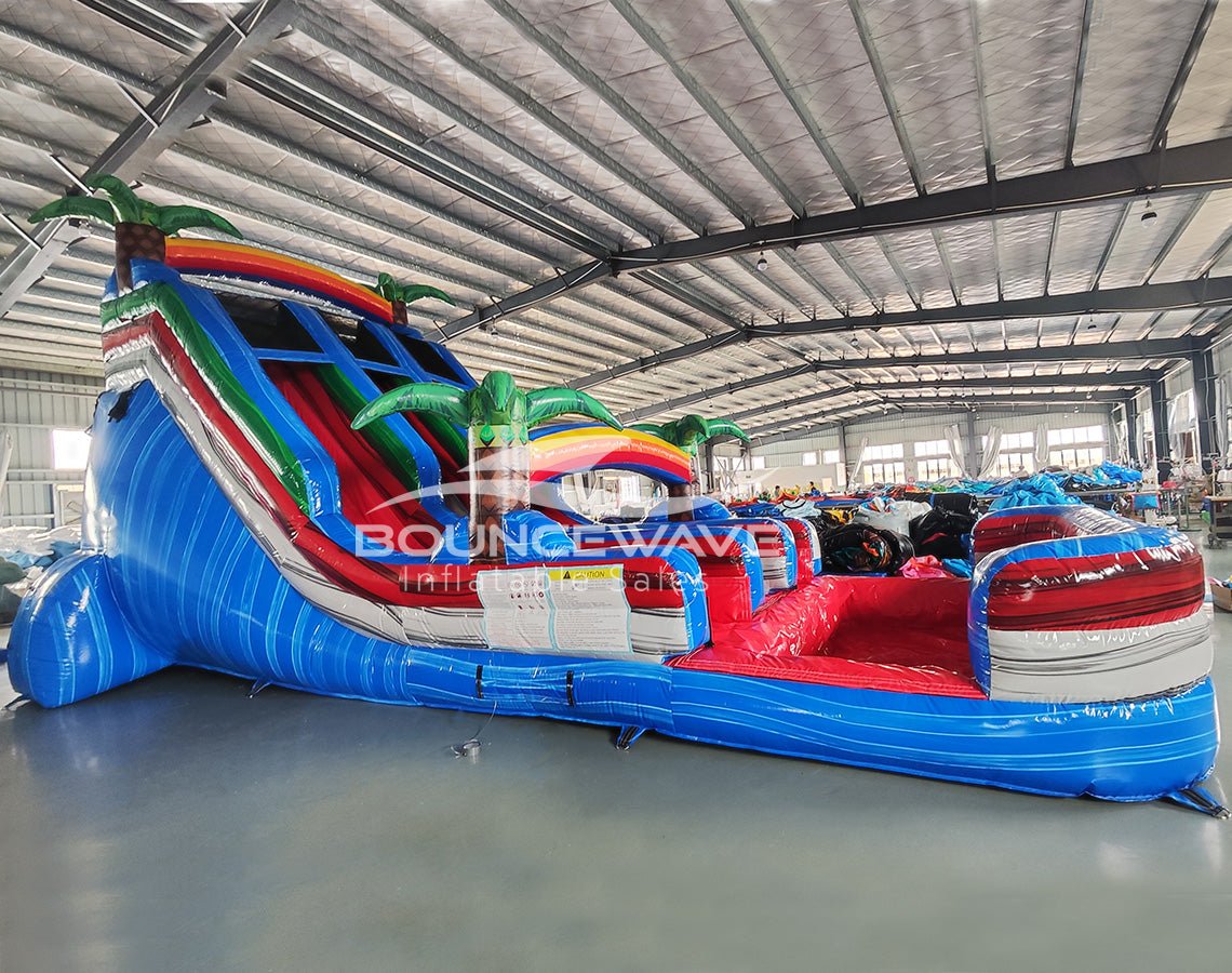 Front view of 18ft Baja Splash Center Climb water slide showing three blue sliding lanes, inflatable palm trees, central climbing area with safety netting, and spacious red and blue splash pool with wave-like patterns.