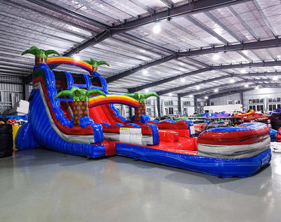 18-foot Baja Splash inflatable water slide in an indoor setting, displaying its towering blue structure, dual lanes, colorful tropical accents, and spacious splash area for all-weather use