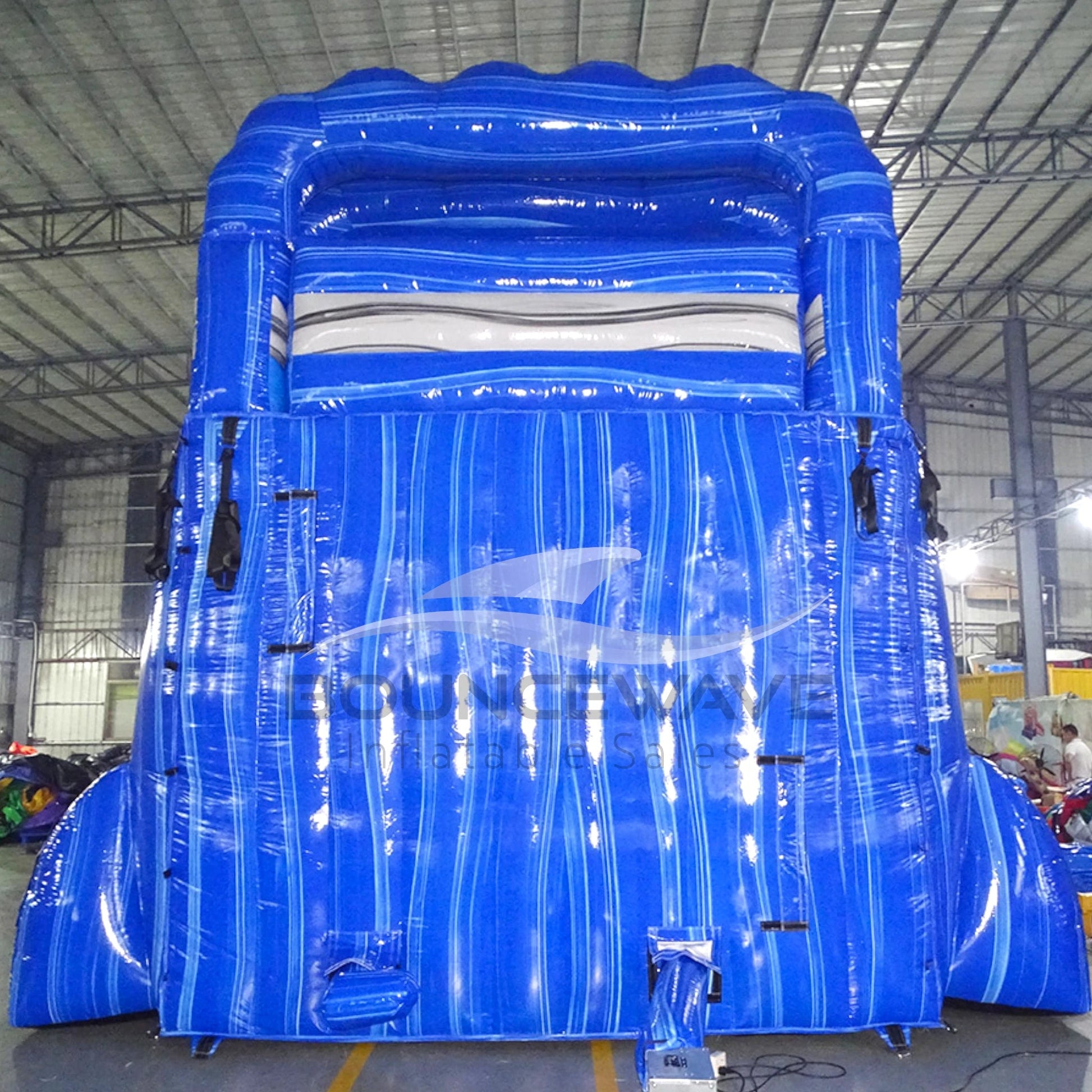 18-foot Blue Lagoon inflatable water slide with dual lanes, featuring a tall blue structure, wave-like design, and a large splash pool at the base for outdoor water entertainment