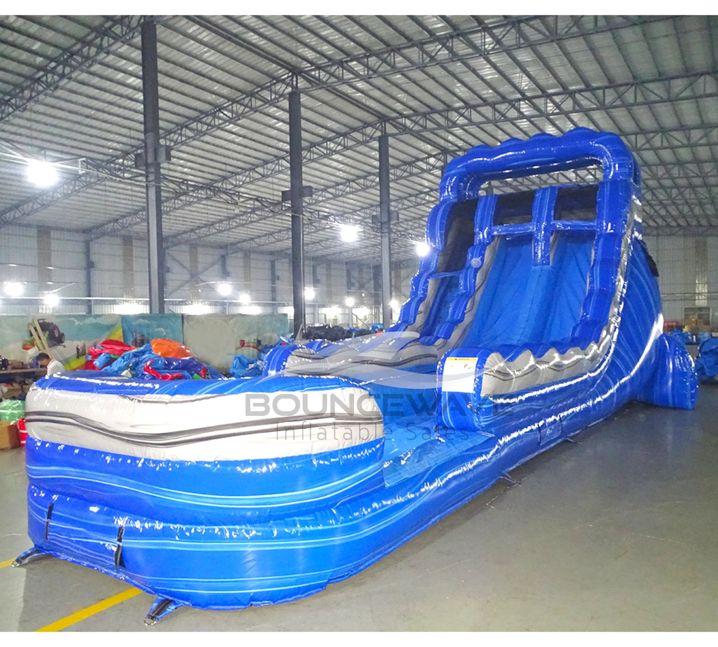 Side view of the 18-foot Blue Lagoon inflatable waterslide, showcasing its height, dual sliding lanes, vibrant blue color scheme, and extended splash area with white accents