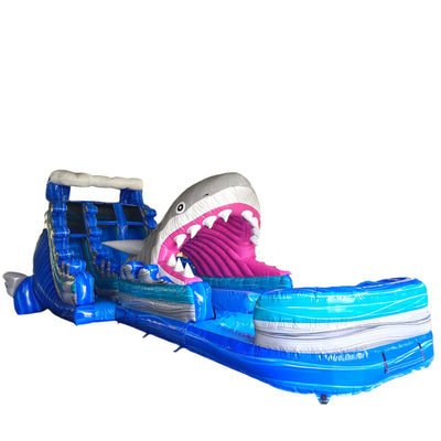 18-foot Cayman Shark Attack inflatable water slide featuring a giant shark head with open jaws, dual blue sliding lanes, and a large splash pool. This thrilling waterslide combines an ocean theme with exciting aquatic entertainment, perfect for outdoor events and parties