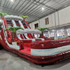 Front angled view of 18ft Crimson Bay water slide showcasing three red sliding lanes with blue wave patterns, green palm tree decorations, and central climbing structure in a spacious indoor facility.