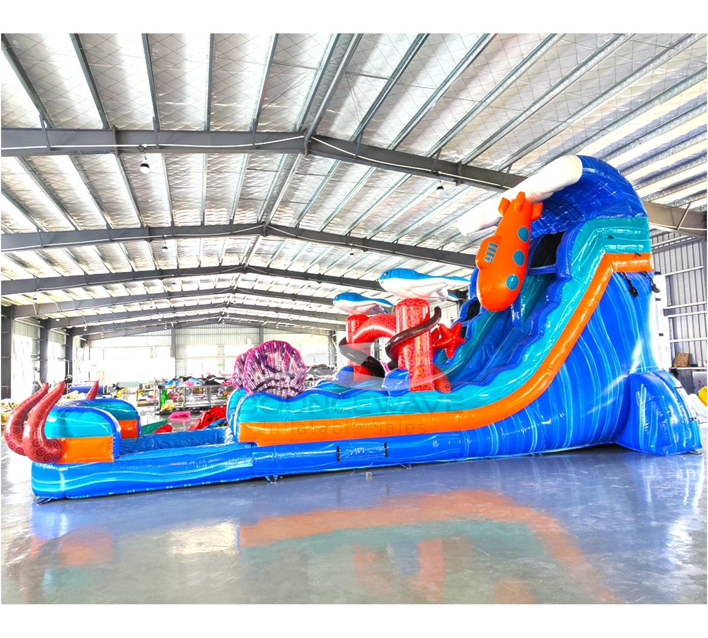 Side angle view of the 18-foot Deep Sea Dive hybrid inflatable water slide in an indoor setting, displaying its impressive size, dual sliding lanes, underwater theme with sea creature decorations, and extended splash pool area.