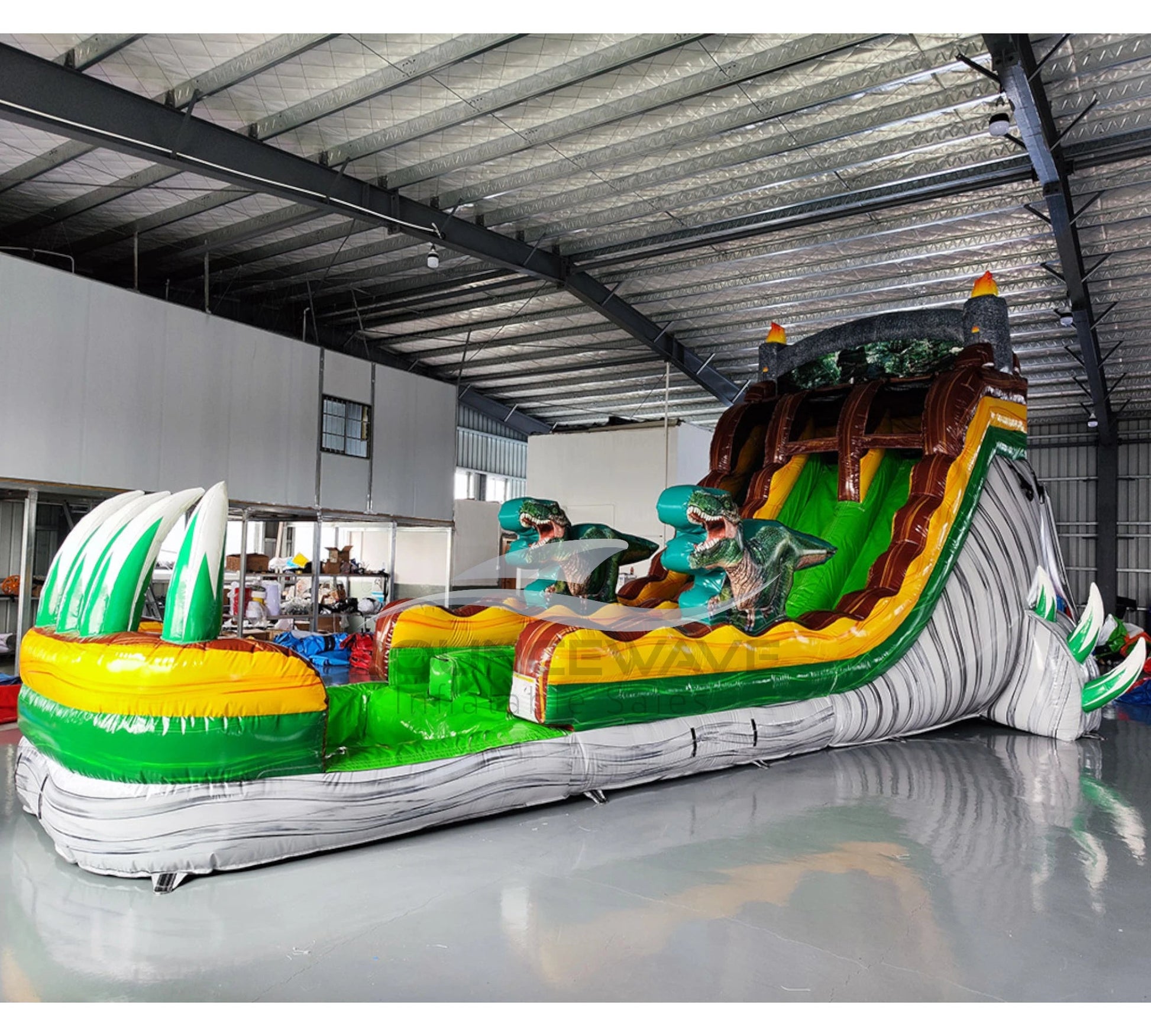 Side view of dinosaur-themed inflatable water slide in indoor setting, showing height and prehistoric design.