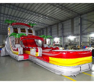 Large tropical-themed inflatable water slide with dual lanes, palm tree decorations, and red, yellow, and white color scheme.