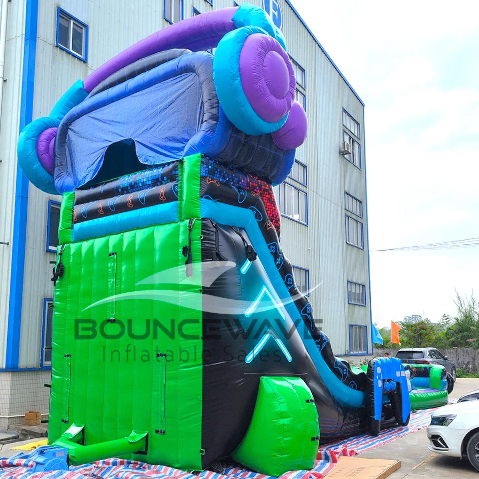 Rear view of gaming-themed inflatable water slide displaying tall structure with green base, colorful top section, and VR headset design.