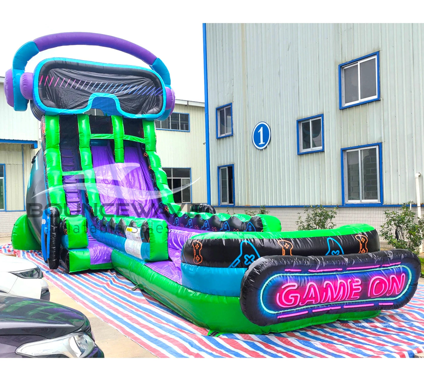 Side view of gaming-themed inflatable water slide showing tall structure with dual sliding lanes and neon-style Game On sign at the base.