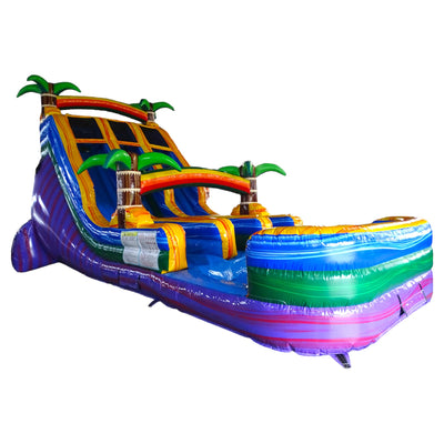 Large inflatable water slide with tropical theme, featuring three blue sliding lanes, yellow borders, palm tree decorations, and a rainbow arch, set up in an indoor warehouse with a colorful splash pool.