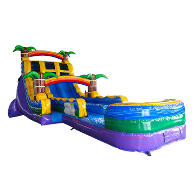 Large tropical-themed inflatable water slide with colorful design, featuring dual lanes, palm tree decorations, and a curved splash pool at the base.