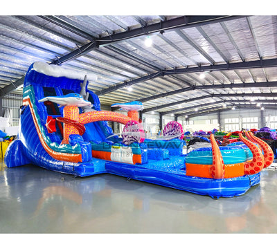 Large ocean-themed inflatable water slide with blue base, featuring shark decorations, dual lanes, and extended splash pool with octopus tentacles.