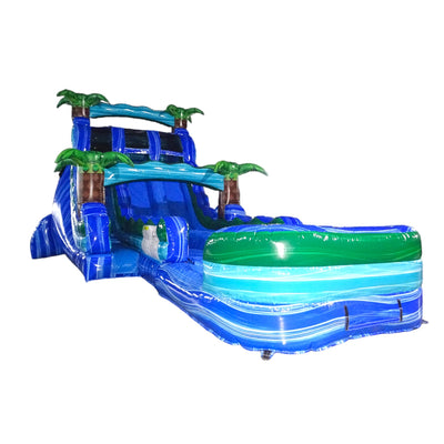 Large tropical-themed inflatable water slide with blue base, featuring dual lanes, palm tree decorations, and an extended splash pool with wave design.