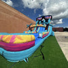 Outdoor view of Island Flow hybrid water slide with sunglasses design, displaying dual lanes, palm trees, and extended splash pool on artificial turf.